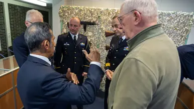 Alttekst: Links: een groep mannen luistert naar een man in uniform op een podium. Rechts: 2 mannen in uniform kijken naar een munt in hun handpalm met drie man om zich heen. 