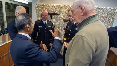 Alttekst: Links: een groep mannen luistert naar een man in uniform op een podium. Rechts: 2 mannen in uniform kijken naar een munt in hun handpalm met drie man om zich heen. 