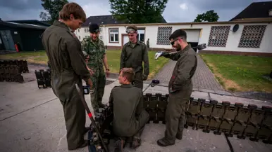 Vijf militairen in overall staan bij een ijzeren constructie. Twee hebben een veiligheidsbril op en een moker in de hand.