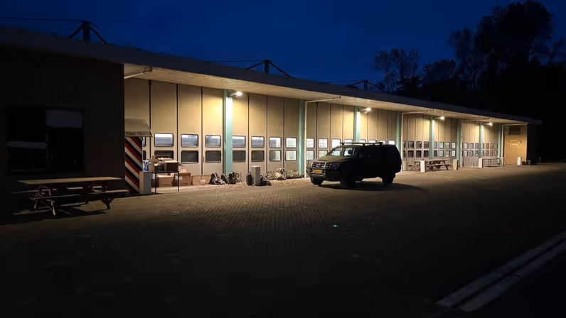 Alttekst: Een militair voertuig staat in het donker geparkeerd voor een loods. 