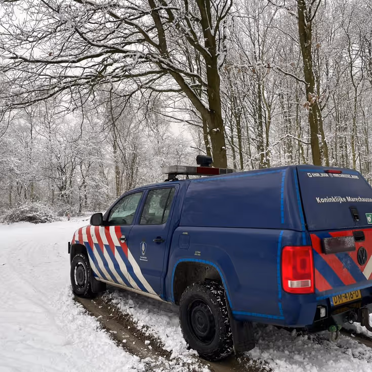 Voertuig van de Marechaussee in een besneeuwd bos.