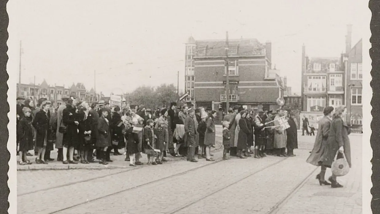 Een groep mensen staat in een rij op een tramhalte, wachtend bij een tramspoor in een oude stad.