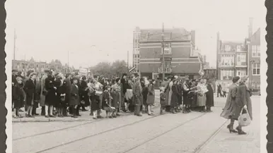 Een groep mensen staat in een rij op een tramhalte, wachtend bij een tramspoor in een oude stad.