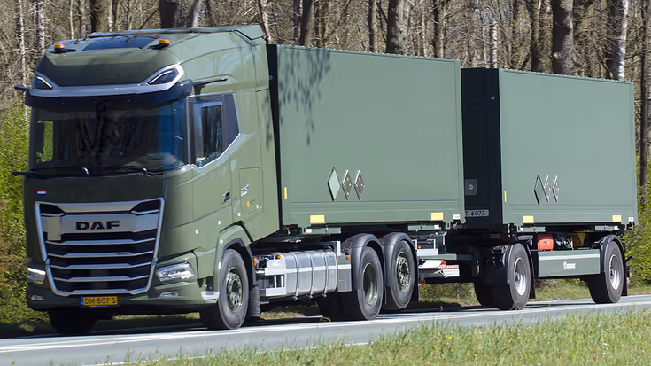 Een groene DAF vrachtwagen met twee aanhangers rijdt over een weg, omringd door bomen en gras.
