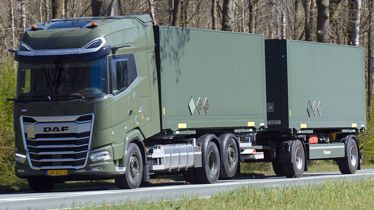 Een groene DAF vrachtwagen met twee aanhangers rijdt over een weg, omringd door bomen en gras.