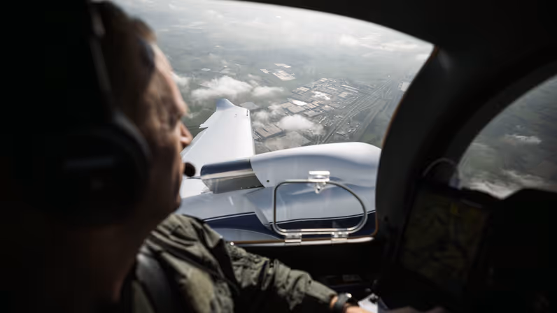  Vlieger van de Koninklijke Marechaussee kijkt tijdens een vlucht vanuit de cockpit over een industriegebied.