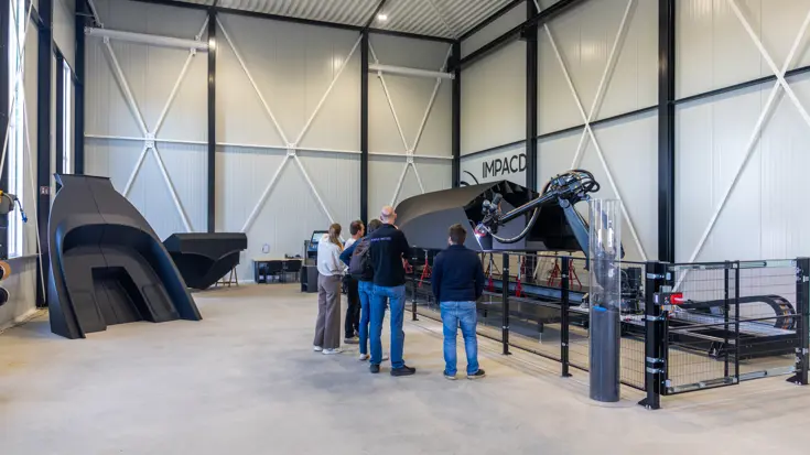  Vijf mensen kijken in fabriekshal naar de 3D-geprinte boot.
