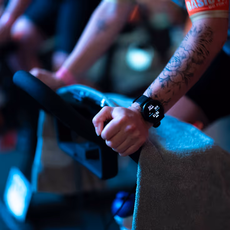 Close up van sporthorloge en handen op het stuur van een indoorbike.