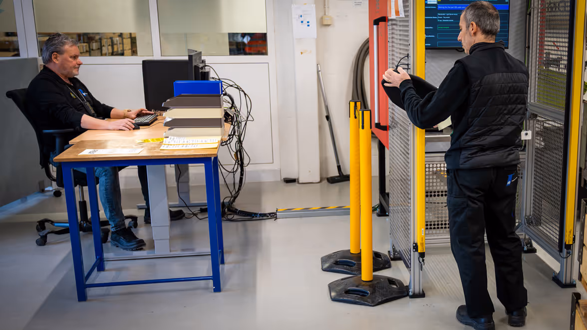 Twee man bezig met het keuren van ballistische platen. Één achter een computerscherm en één bij de scanner.