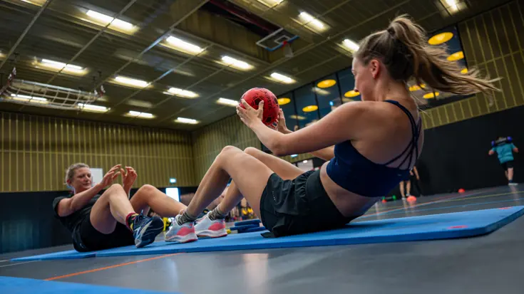 twee werkneemsters gooien een bal over in een sportzaal
