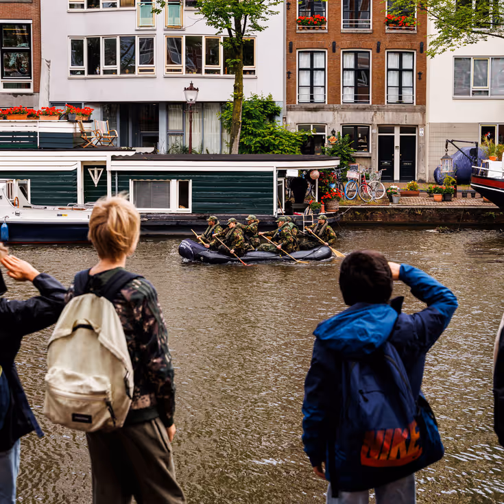 De deelnemers aan de NWT roeien in rubberboten door Amsterdam.