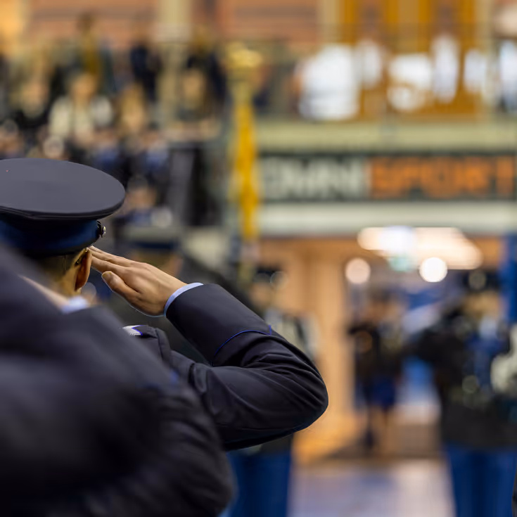 Marechaussees in ceremonieel tenue staan in de houding, met op de achtergrond wazig een bordje met daarop de naam van de sporthal, Omnisport.