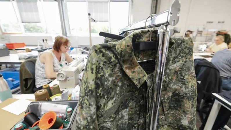 Een militair kledingstuk hangt aan een rek in een atelier. Bijschrift: Hexonia heeft een speciale ruimte waar voor elk onderdeel van de gevechtskleding een prototype kan worden gemaakt. Handig voor testen en kortcyclische doorontwikkeling. 