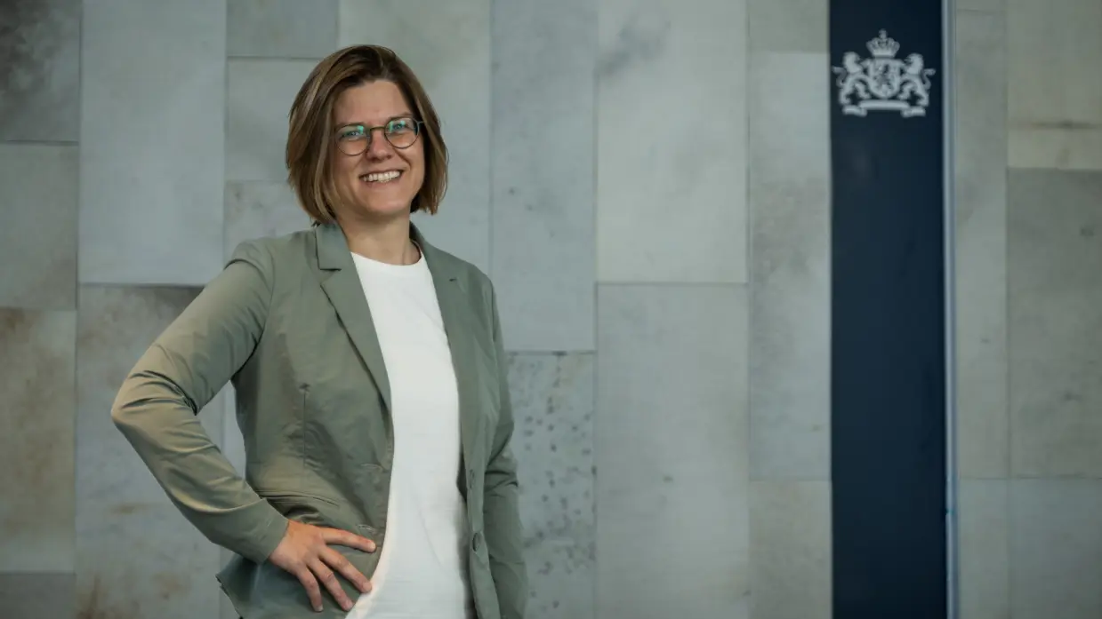 Bebrilde vrouw in groen jasje en wit shirt poseert lachend.