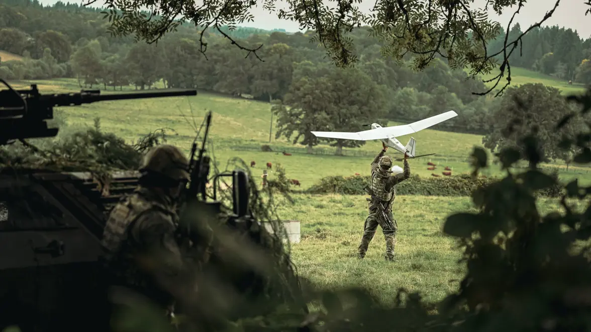 Een militair werpt een drone in een bosrijke omgeving.