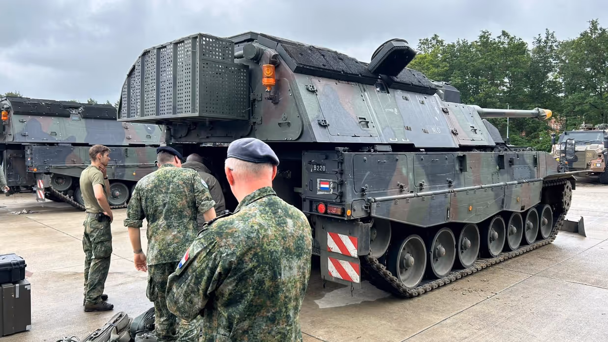 Vier personen in militaire kledij inspecteren een militair voertuig.