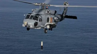 Een helikopter vliegt boven een kalme zee en laat een projectiel zakken aan een touw.
