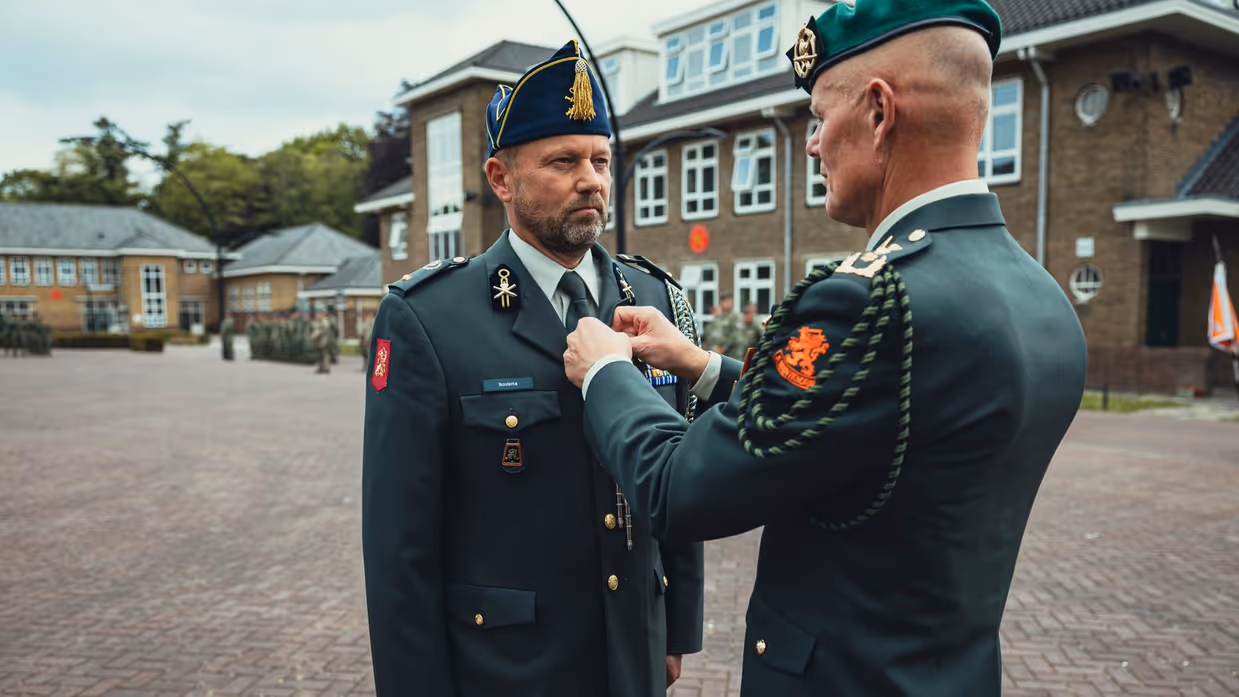Generaal Swillens bevestigt een koord of iets dergelijks aan het DT-jasje van de adjudant Klaas Bootsma. 