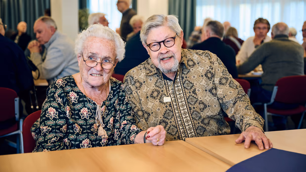 Een vrouw en een man lachen en zitten aan een tafel.