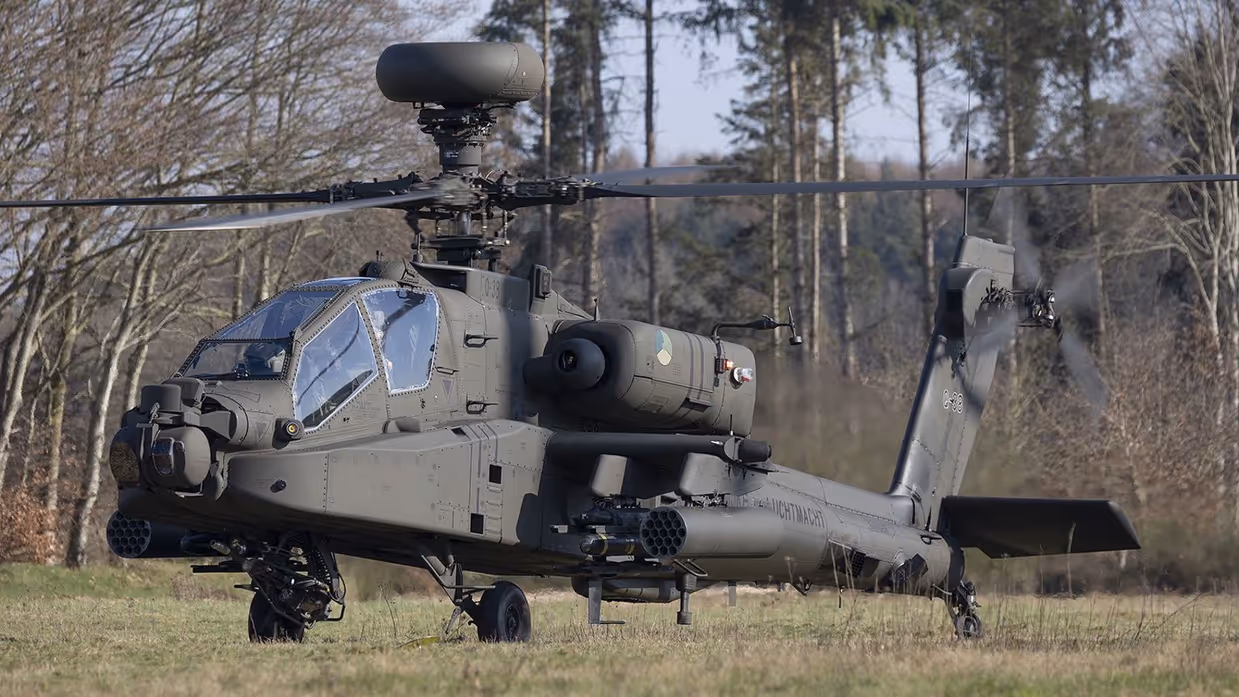 Een zwarte gevechtshelikopter met zware bewapening en draaiende rotorbladen staat op een grasveld tussen kale bomen in een bosrijke omgeving. Rechts: Een militaire helikopter vliegt laag boven een open veld, veroorzaakt stofwolken met ingeladen wapens en draaiende rotorbladen tussen kale bomen.