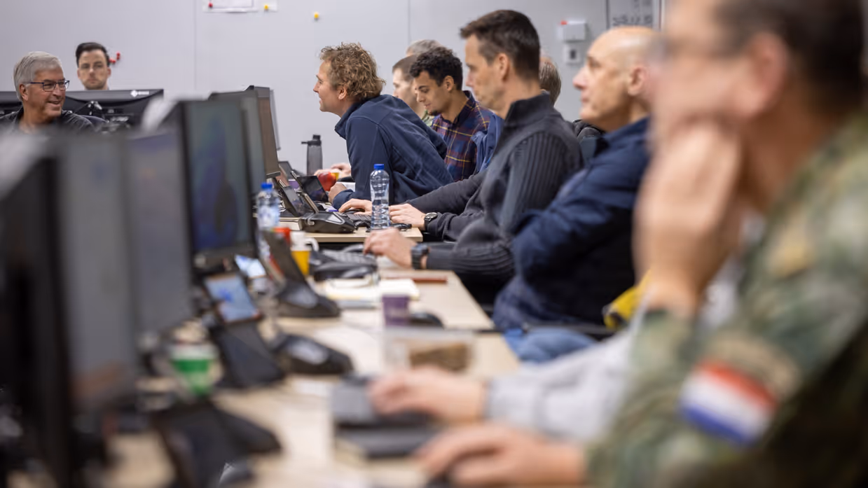 Twee personen die achter elkaar zitten zijn met elkaar in gesprek. Daarbij lachen ze.