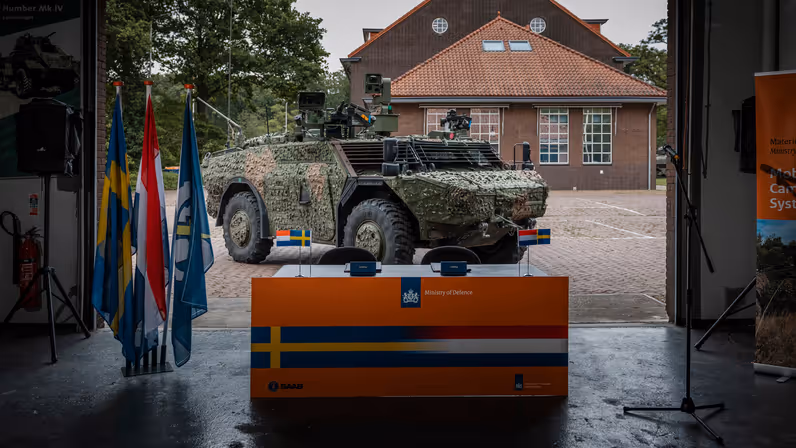  Een officiële tekentafel met daarachter een militair voertuig. 