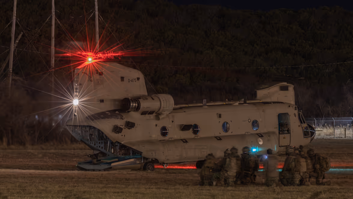 In duisternis groepje knielende militairen naast een Chinook met openstaande achterklep.