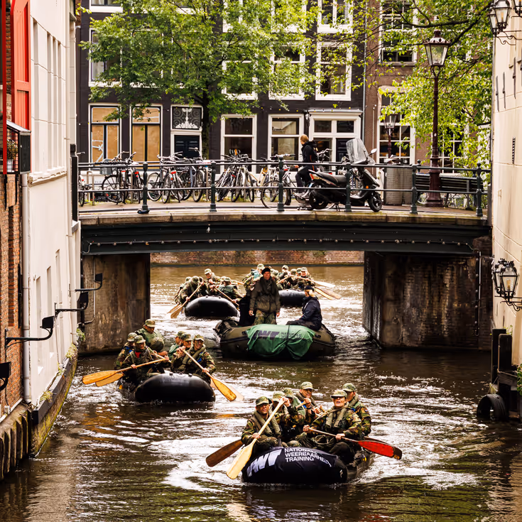 De deelnemers aan de NWT roeien in rubberboten door Amsterdam.