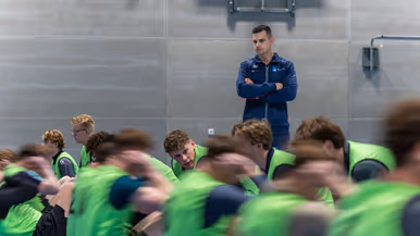 Jongeren in gele hesjes voeren diverse sportonderdelen uit in een sportzaal. 