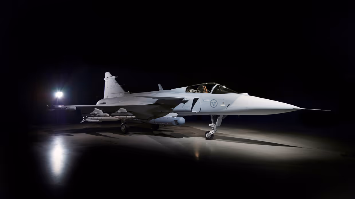 Een straaljager in een donkere hangar, verlicht door een felle lamp. Het vliegtuig staat stil op de grond, met een slanke, puntige neus en wapens onder de vleugels. 