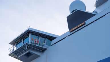 Een grijze kraan op het dek van het schip, een donkergrijze reddingsboot en het predicaat met daarop ‘Den Helder’.