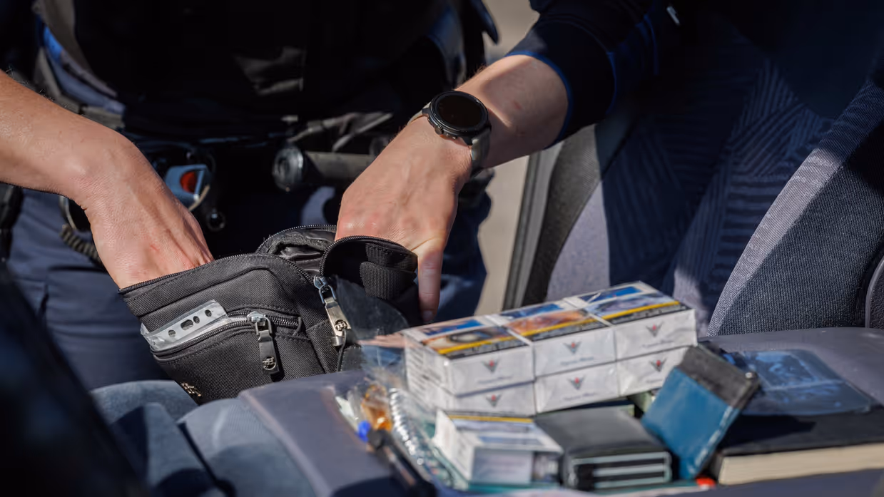 Iemand doorzoekt de inhoud van een tas, sigaretten en portemonnee liggen op de voorgrond.