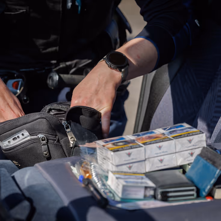 Iemand doorzoekt de inhoud van een tas, sigaretten en portemonnee liggen op de voorgrond.