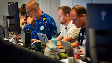 Burgermedewerkers en een marineman werken achter hun eigen beeldscherm.