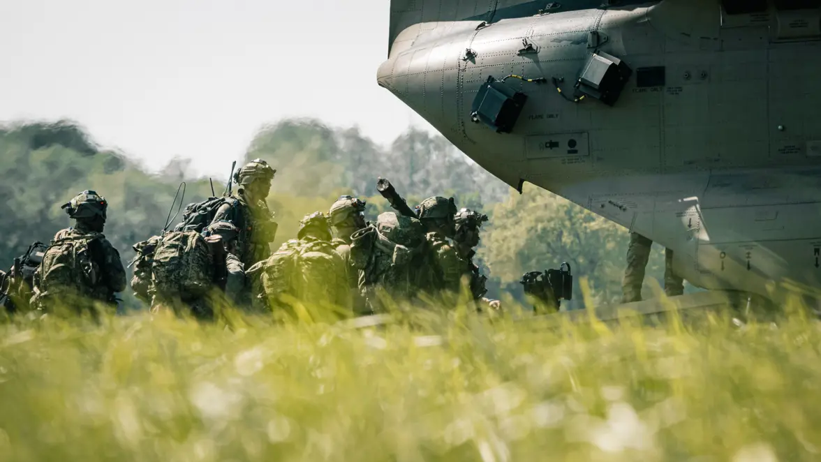 Militairen met volledige uitrusting verzamelen zich in een grasveld naast een militair transportvliegtuig tijdens oefening Falcon Leap.