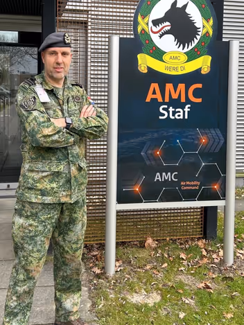 Portretfoto van luitenant-kolonel Misja Woudt. Naast hem het logo van het Air Mobility Command in Eindhoven.