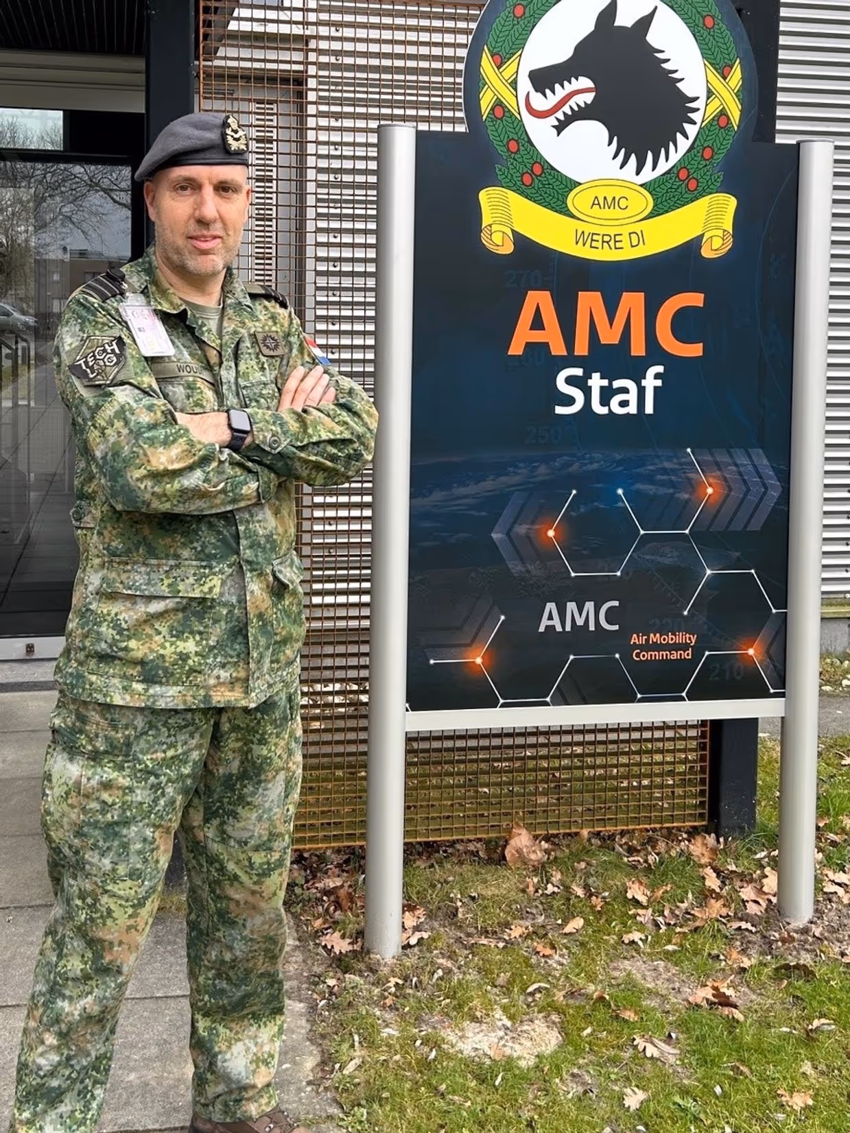 Portretfoto van luitenant-kolonel Misja Woudt. Naast hem het logo van het Air Mobility Command in Eindhoven.