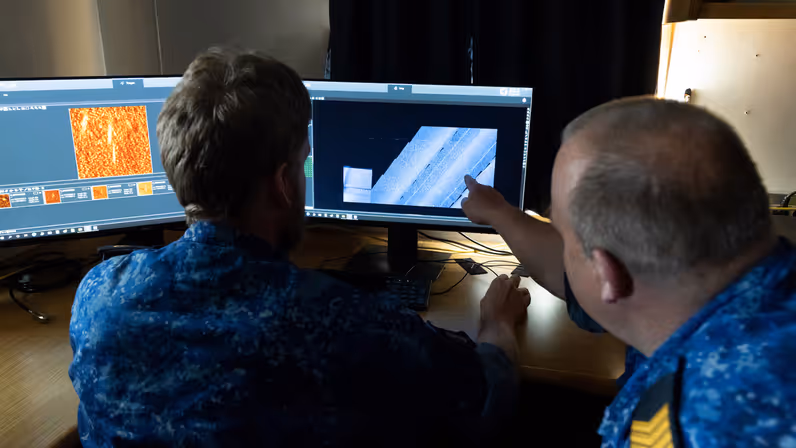 Twee marinecollega’s kijken naar een scherm met onderwaterbeelden. 