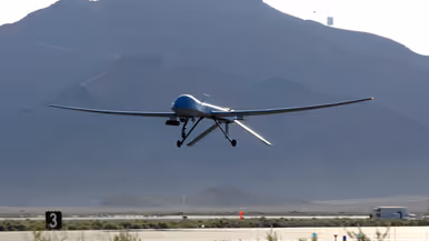 Vlak boven een startbaan vliegende MQ-1. Op de achtergrond een berg.