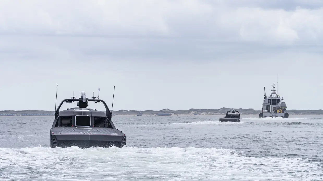 Twee onbemande boten varen op zee achter schip aan.