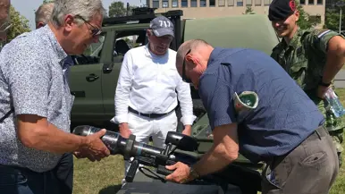  Een militair met een groot wapen wordt omringd door een aantal mensen.