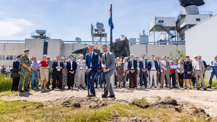 Een aantal burgers en militairen. Twee mensen steken een schop in de grond.