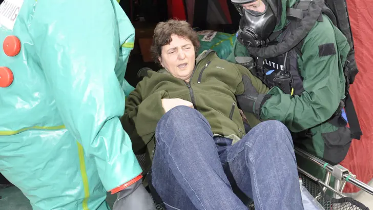 Vrouw wordt op een brancard een tent in gedragen door personen in beschermende pakken.