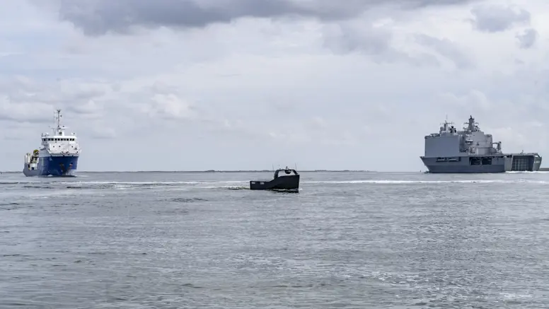 Klein onbemand bootje vaart tussen 2 grote schepen op zee.