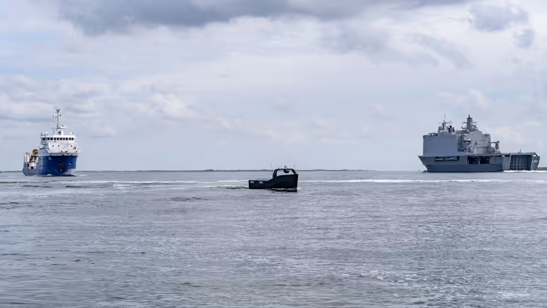Klein onbemand bootje vaart tussen 2 grote schepen op zee.