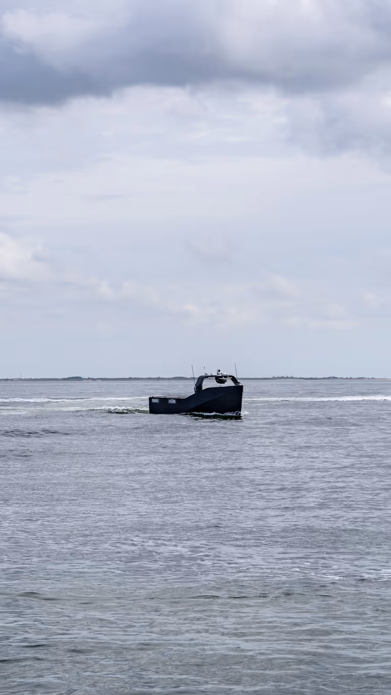 Klein onbemand bootje vaart tussen 2 grote schepen op zee.