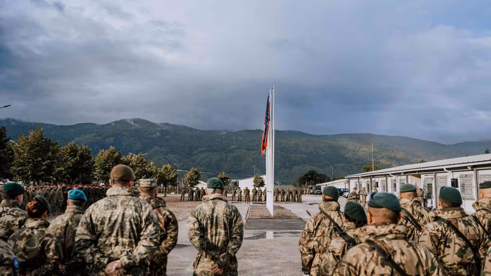 Infanteristen op  de rug gezien met een vlag op de achtergrond en daarachter heuvels.