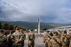 Infanteristen op  de rug gezien met een vlag op de achtergrond en daarachter heuvels.