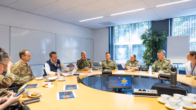 Popolo en Adang samen met nog een aantal militairen en een burger in gesprek aan een ronde tafel.