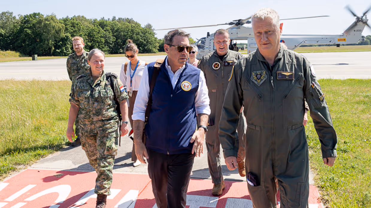 Popolo lopend in gesprek met Commandant Air Combat Command commodore Marcel van Egmond. Achter hen loopt een aantal militairen en burgers met op de achtergrond een NH90. 